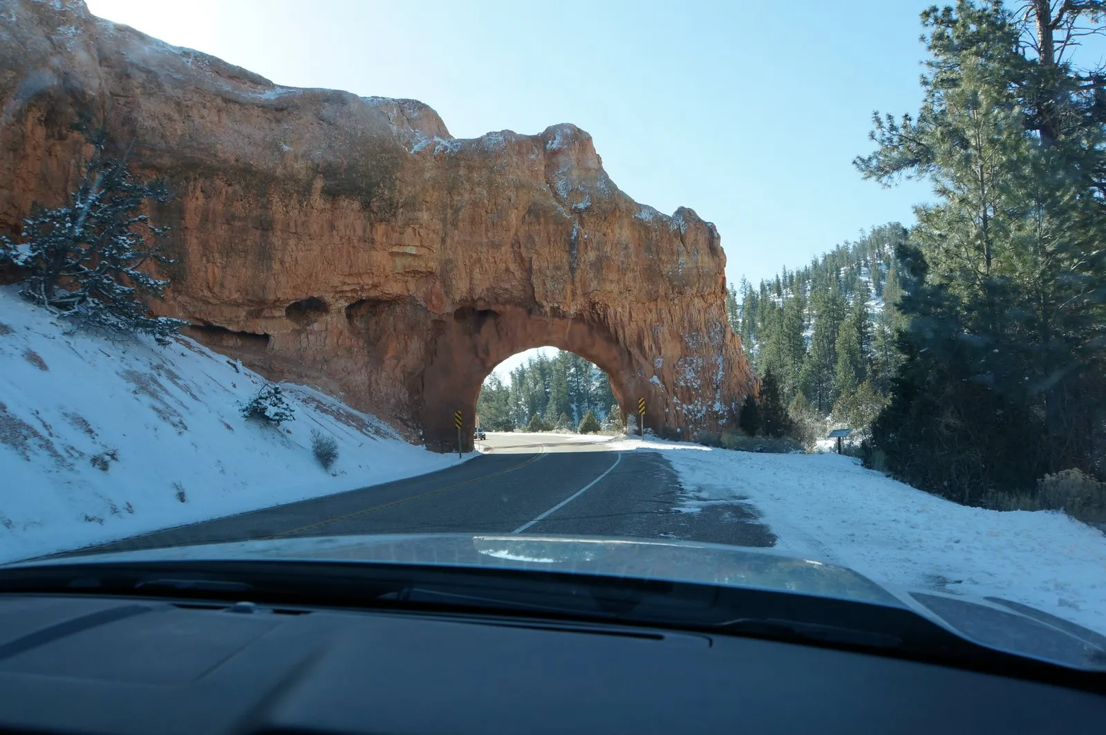 Snowy mountain road leading through a red rock arch