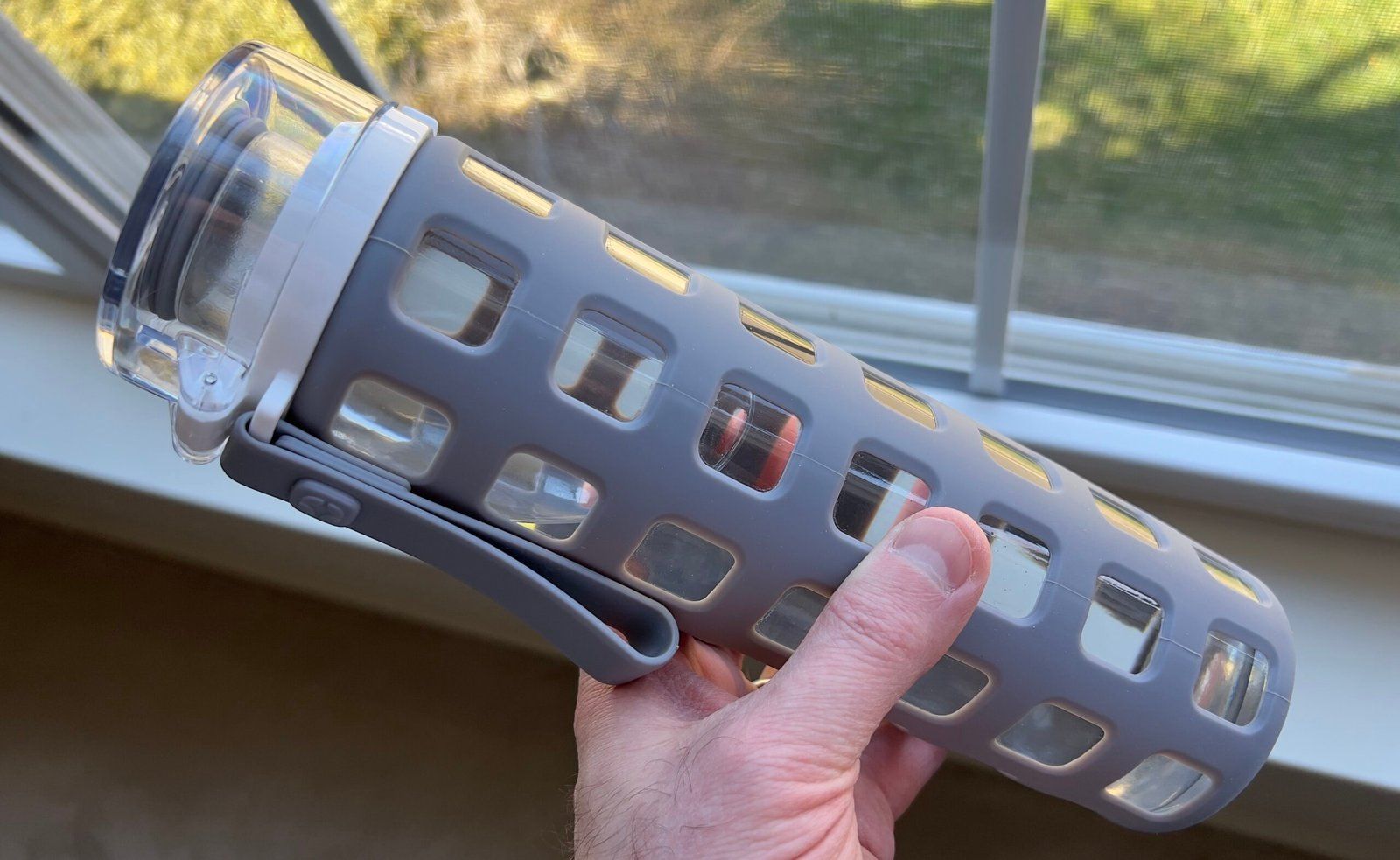 Hand holding a reusable glass water bottle with a silicone sleeve